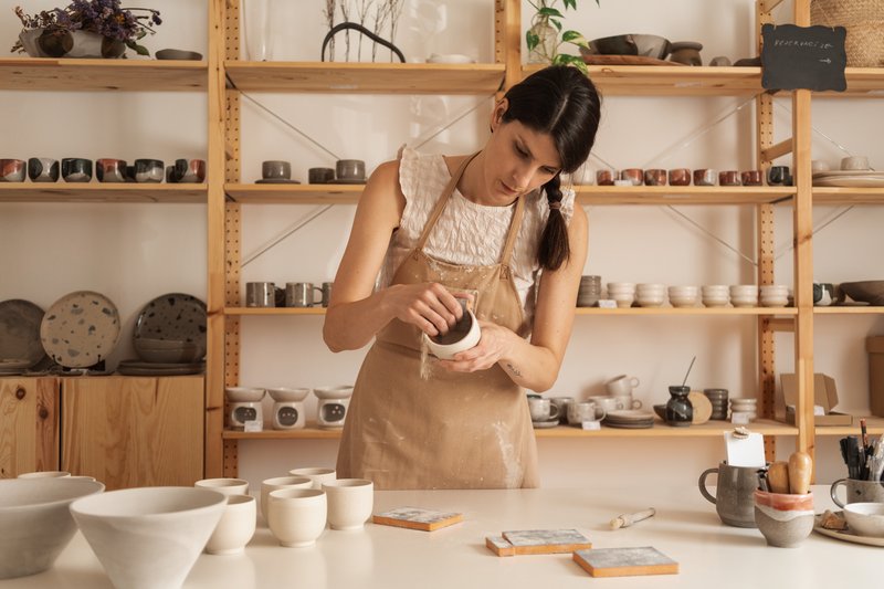 A ceramicist at her wheel in a small studio, working clay on the wheel head