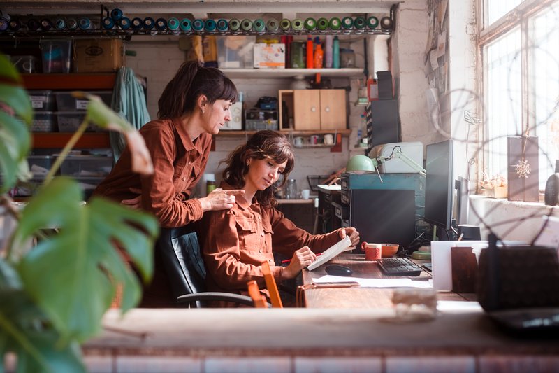 Two collaborators reviewing paperwork at a desk in their small studio office