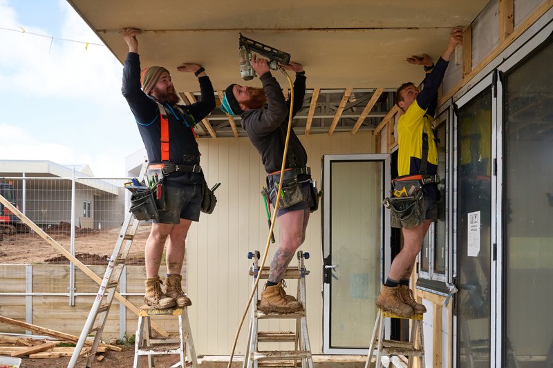 Three tradespeople in hi-vis working on the eaves of a building